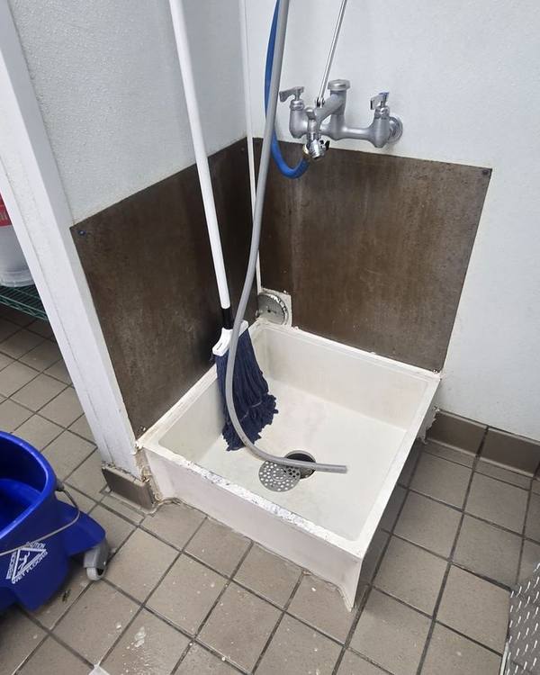 Mop sink with an old rusted backsplash panel