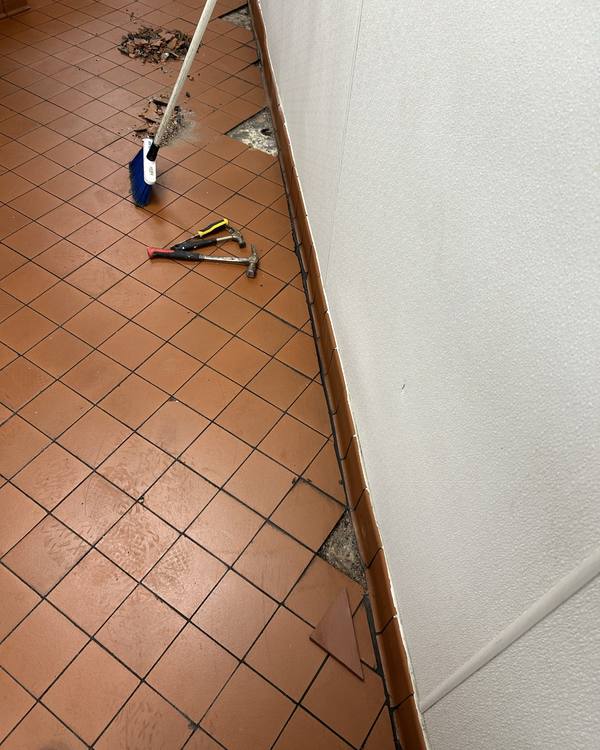 Broken floor tiles along a kitchen wall