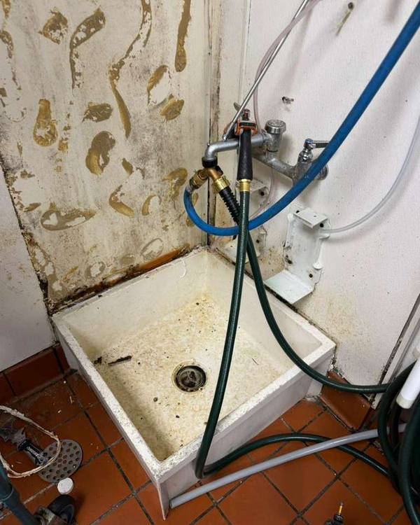 Commercial mop sink before renovation, with stained walls and worn floor