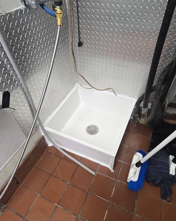 New white mop sink installed with metal wall panels and clean tile floor